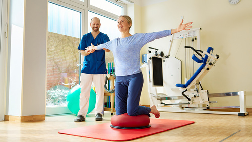 Physiotherapeut und Patientin bei einer Gleichgewichtsübrung auf Bodenmatte und Ball.